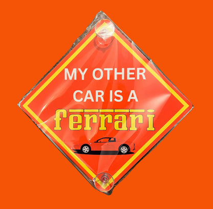 Red aluminium car window sign with text 'My Other Car is a Ferrari' and sports car graphic. Fun and durable vehicle accessory for drivers.